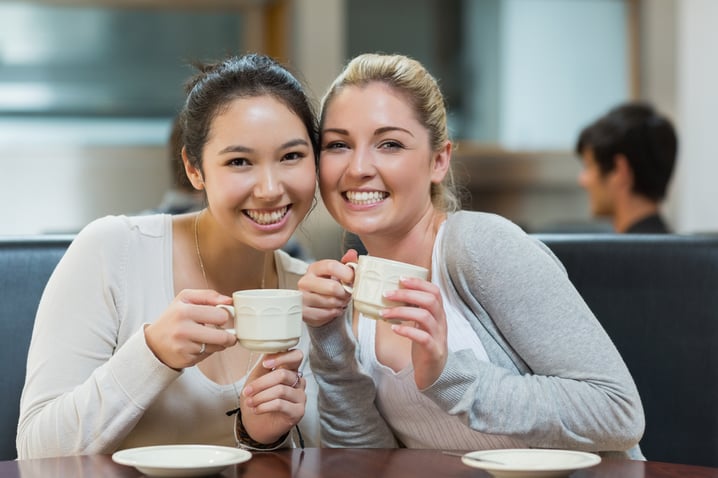 Two students sitting in college coffee shop while drinking and holding a cup of coffee